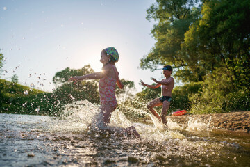 Happy children run from the shore into the water. Summer children's vacation on shore of a lake or...