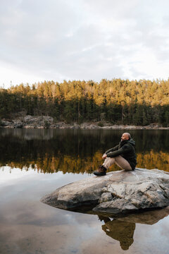 Manlig vandrare sitter p&aring; klippa vid sj&ouml; och funderar