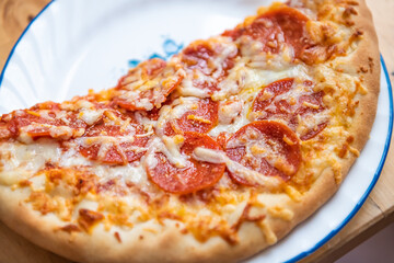 Fresh thin crust half a pizza on plate with melted mozzarella cheese, pepperoni meat slices macro closeup of greasy food