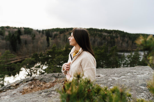 Ung kvinna st&aring;r p&aring; klippa i skog och tittar bort