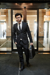 Fototapeta premium Vertical full length portrait of successful Middle-Eastern businessman entering hotel lobby on business trip