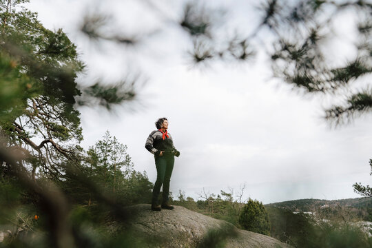 Kvinna st&aring;r p&aring; klippa i skog och tittar bort