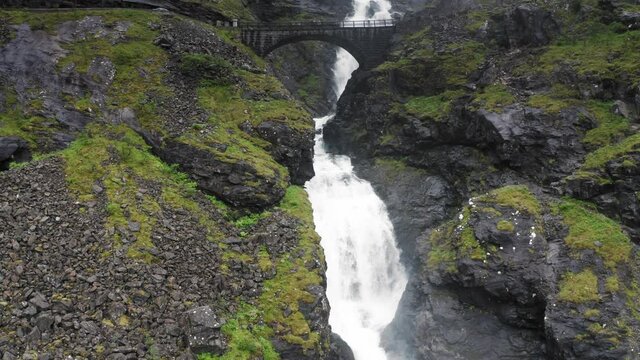 Going up the mountain where a beautiful waterfall Stigfossen is running down the hill, white water is noisily falling under a stone arch bridge, and lush green moss is covering the slopes.