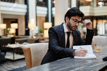 Portrait of successful Middle-Eastern businessman working in hotel lobby during business trip, copy space