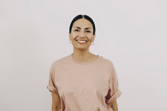 Portr&auml;tt av glad kvinna med rosa t-shirt framf&ouml;r vit bakgrund