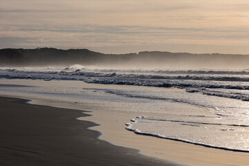 Sunrise at the beach with mountains and waves crashing in the background