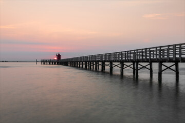 Fototapeta premium Alba al faro rosso di Lignano, paesaggio sul mare con passeggiata pedonale.