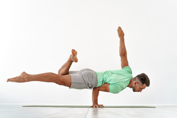 Man practicing balance yoga pose on white studio background