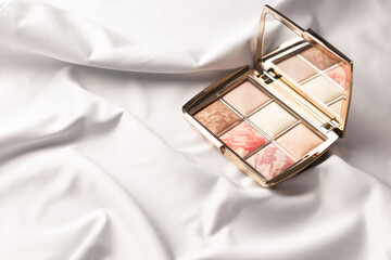 Luxury eyeshadow palette, eye shadows cosmetics product on white silk cloth. Textile background, drapery and pleats on delicate fabric. Copy space. MUA and girly concept. Make-up palette close-up