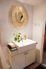 Simple powder room with vanity sink. There is rattan bamboo mirror on the wall, white countertop and cabinet, there is green vine plants pot
