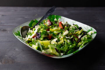 Fresh salad with vegetables in bowl with spoon on black wooden table
