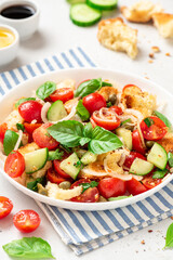 Panzanella - Italian salad from vegetables and bread. Salad with tomatoes, onions, cucumbers, bread, capers and basil in a white plate on a gray concrete background. Vegan salad, Italian cuisine
