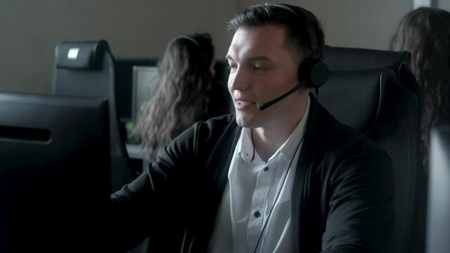 Operator is young man working in call center for VIP customer service. agent puts on headset looks at monitor and helps clients. Service and online security with support of dispatcher from the office