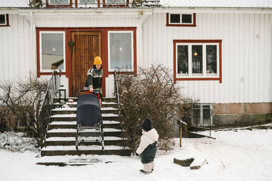 Mamma b&auml;r barnvagn i trappa medan dotter st&aring;r bredvid