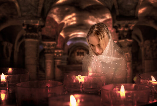 mujer rezando con velo blanco delante de velas encendidas