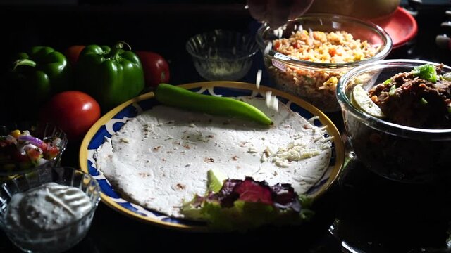 slow motion shot of cheese being dropped on top of a flat bread for a taco tortilla fajita with the sides of fresh vegetables like tomatos bell peppers chillies and rice in dramatic light
