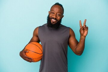 African american man playing basketball isolated on blue background joyful and carefree showing a peace symbol with fingers.