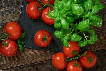 Fresh  ripe red tomatoes on a cutting board with fresh basil on a wooden background. Freshly picked red tomatoes and basil  leaves for cooking. top view