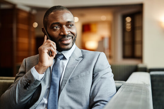 Portrait of smiling African-American businessman speaking by smartphone at hotel lobby during business trip, copy space