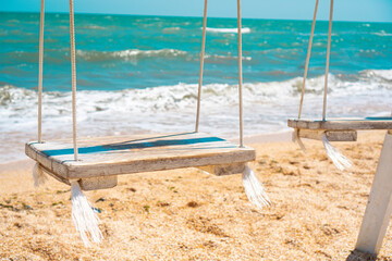 Fototapeta na wymiar Swings with a wooden seats against the blue sea