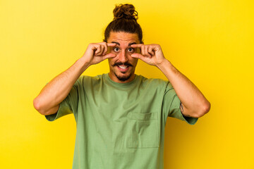 Fototapeta premium Young caucasian man with long hair isolated on yellow background keeping eyes opened to find a success opportunity.