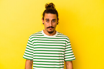 Young caucasian man with long hair isolated on yellow background sad, serious face, feeling...