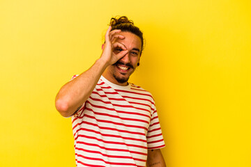 Young caucasian man with long hair isolated on yellow background excited keeping ok gesture on eye.