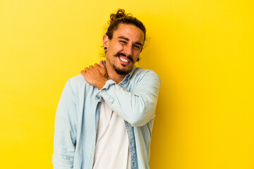 Young caucasian man with long hair isolated on yellow background having a shoulder pain.