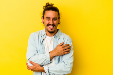 Young caucasian man with long hair isolated on yellow background massaging elbow, suffering after a bad movement.