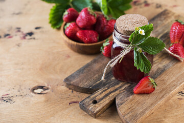 Strawberry jam in a jar on a wooden board. Fermented berries. Copy space.