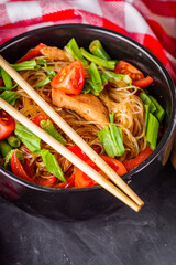 delicious glass noodles with chicken and vegetables on a dark stone background