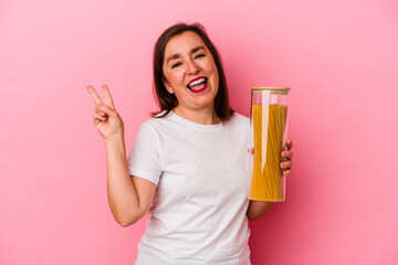 Middle age caucasian woman holding a pasta jar isolated on pink background joyful and carefree showing a peace symbol with fingers.