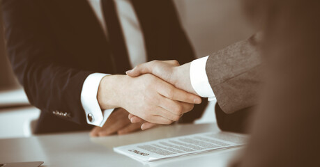 Unknown businessman shaking hands with his colleague or partner above the glass desk in modern office, close-up. Business people group at meeting