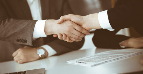 Obraz premium Unknown businessman shaking hands with his colleague or partner above the glass desk in modern office, close-up. Business people group at meeting