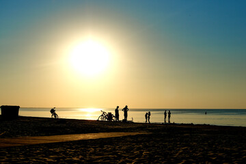 Silhouettes of people and bicycles on the beach against the backdrop of the sunset. Relax on the beach in summer.