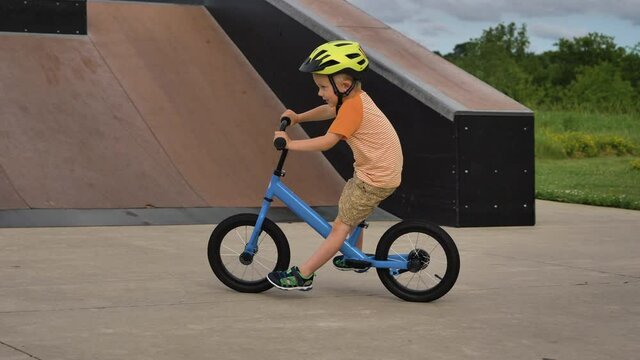 Little boy riding a balance bike in a skatepark, wearing a helmet for safety