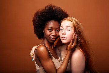 Obraz premium young pretty caucasian, afro woman posing cheerful together on brown background, lifestyle diverse nationality people concept