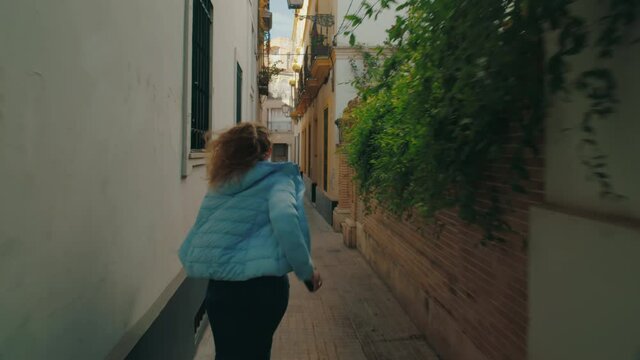 Camera follows young woman when she looks at phone and run late to meeting. Woman run in narrow city street, late for date or appointment. Female traveller running to make it to train or plane