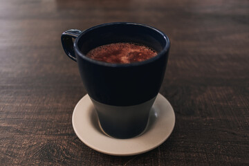 Closeup of hot cocoa drink in blue mug on dark wooden table.