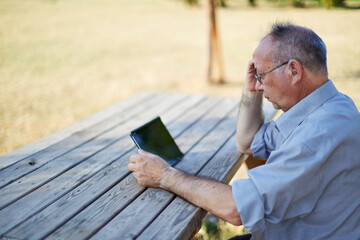 Old man with hearing aid looking tablet outdoor