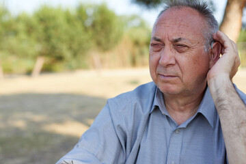 old man with audition problems hand on hearing aid