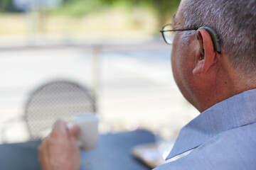 Old man back with hearing aid drinking coffee