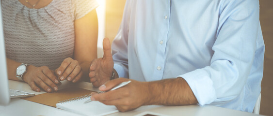 Unknown businessman and woman working with computer in sunny office, close-up. Teamwork, partnership and business concept