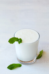 glass of cold dairy Lassi drink with fresh green mint on white background. healthy, fermented products concept. Copy space. Kefir, yogurt or milk with probiotics on the table. Indian cuisine. vertical