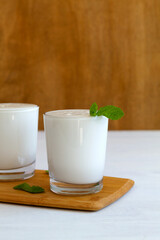 two glass of yogurt with green mint on white table. fresh dairy drink. healthy, fermented products concept. Copy space. Kefir, milk or Lassi drink with probiotics on the table. Indian cuisine.vertical