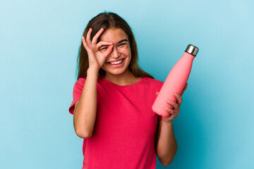 Young caucasian woman holding a water bottle isolated on blue background excited keeping ok gesture...