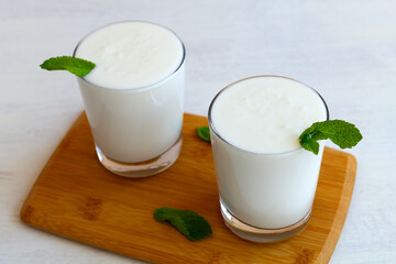 two glass of Lassi drink with green mint on wooden table. close-up fresh dairy drink.healthy, fermented products concept. Copy space.Kefir, milk or yogurt with probiotics on the table. Indian cuisine.