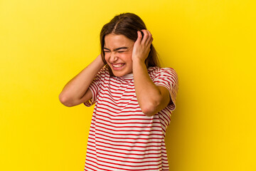 Young caucasian woman isolated on yellow background covering ears with hands.
