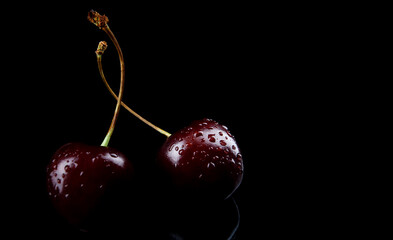 Two cherry berries with drops of water on the peel are isolated on a black background.