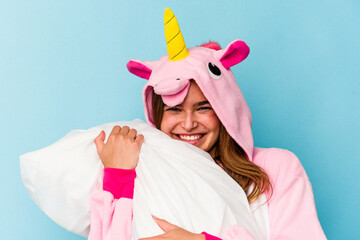 Young caucasian cute woman wearing an unicorn pajama holding a pillow isolated on blue